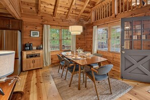 Ein Holzblock-Interieur mit einem Esstisch für vier Personen, einer Küchenzeile und einem großen Fenster mit Vorhängen.