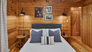 Una camera in una baita di legno con un letto, due comodini, una testiera e due lampade a parete.