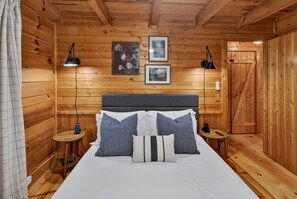 Ein Zimmer einer Holzhütte mit einem Bett, zwei Nachttischen, einem Kopfteil und zwei Wandlampen.