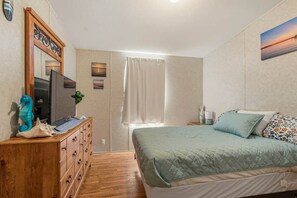 Um quarto com cama, penteadeira, televisão, janela com cortinas e decoração nas paredes.