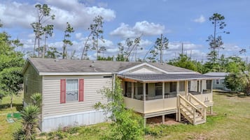 A mobile home with a porch, a small attached structure, and a grassy yard.