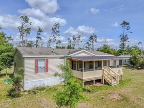 Uma casa móvel com varanda, uma pequena construção anexa e um gramado.