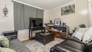 Una sala de estar con sofá, una mesa de centro, un televisor sobre un mueble, una estantería y un cuadro en la pared.