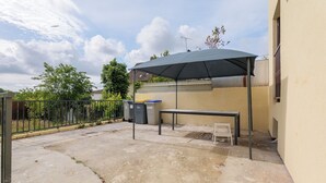 Une terrasse extérieure avec une table et un banc, un espace abrité et des poubelles.