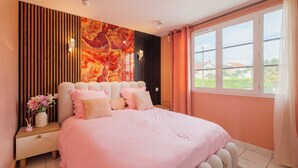 Une chambre à coucher avec un lit, une table de chevet, un vase de fleurs et une grande fenêtre.