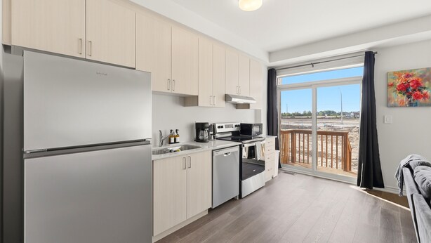 A modern kitchen with a refrigerator, oven, and microwave, a balcony with a view, and a painting on the wall.
