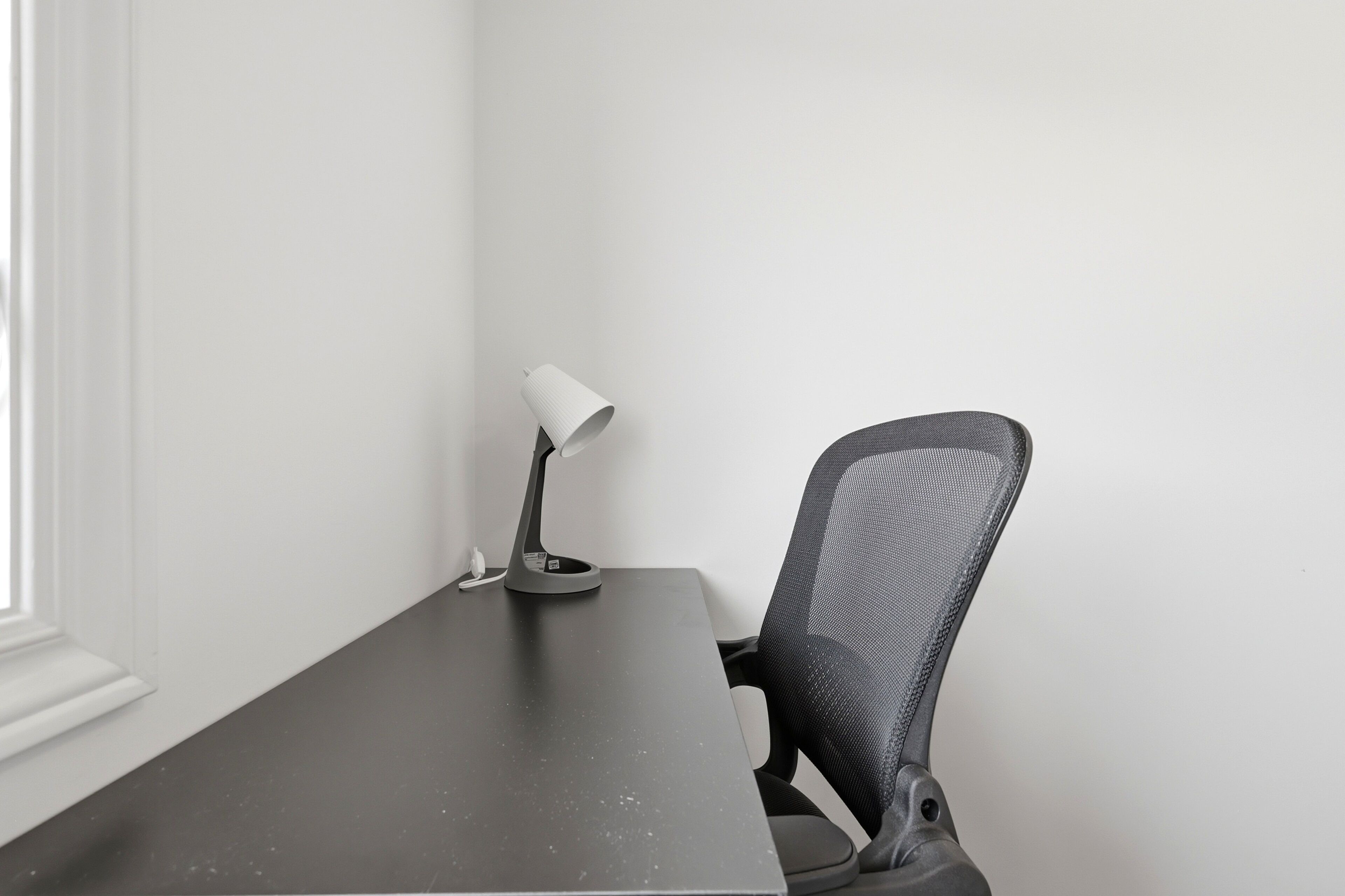 A desk with a lamp and a mesh office chair in a room with white walls.