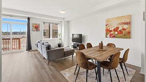 A modern living room with a sofa, dining table, and chairs, a television, and a painting on the wall.