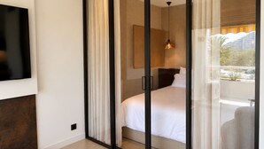 Une chambre dotée d’une porte-fenêtre coulissante, d’un lit, d’un téléviseur fixé au mur et d’un luminaire suspendu.