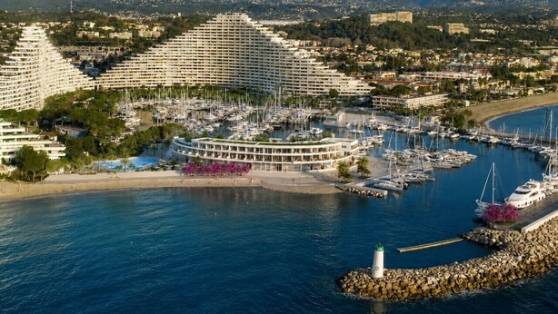 Un port de plaisance avec de nombreux bateaux, un grand hôtel doté d’un bâtiment circulaire et une zone de plage.