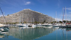 Un port de plaisance où sont amarrés de nombreux yachts dans des eaux calmes, un grand bâtiment d’hôtel en arrière-plan et un ciel dégagé.