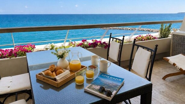 Una mesa con alimentos para el desayuno, una revista y vista al mar.