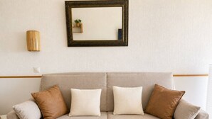 A beige sofa with four cushions, a wall-mounted mirror, and a small shelf with a plant. - Cocon Marina—Baie des Anges (Villeneuve-Loubet)