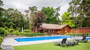 A pool area with lounge chairs, a wooden building, and surrounding greenery.