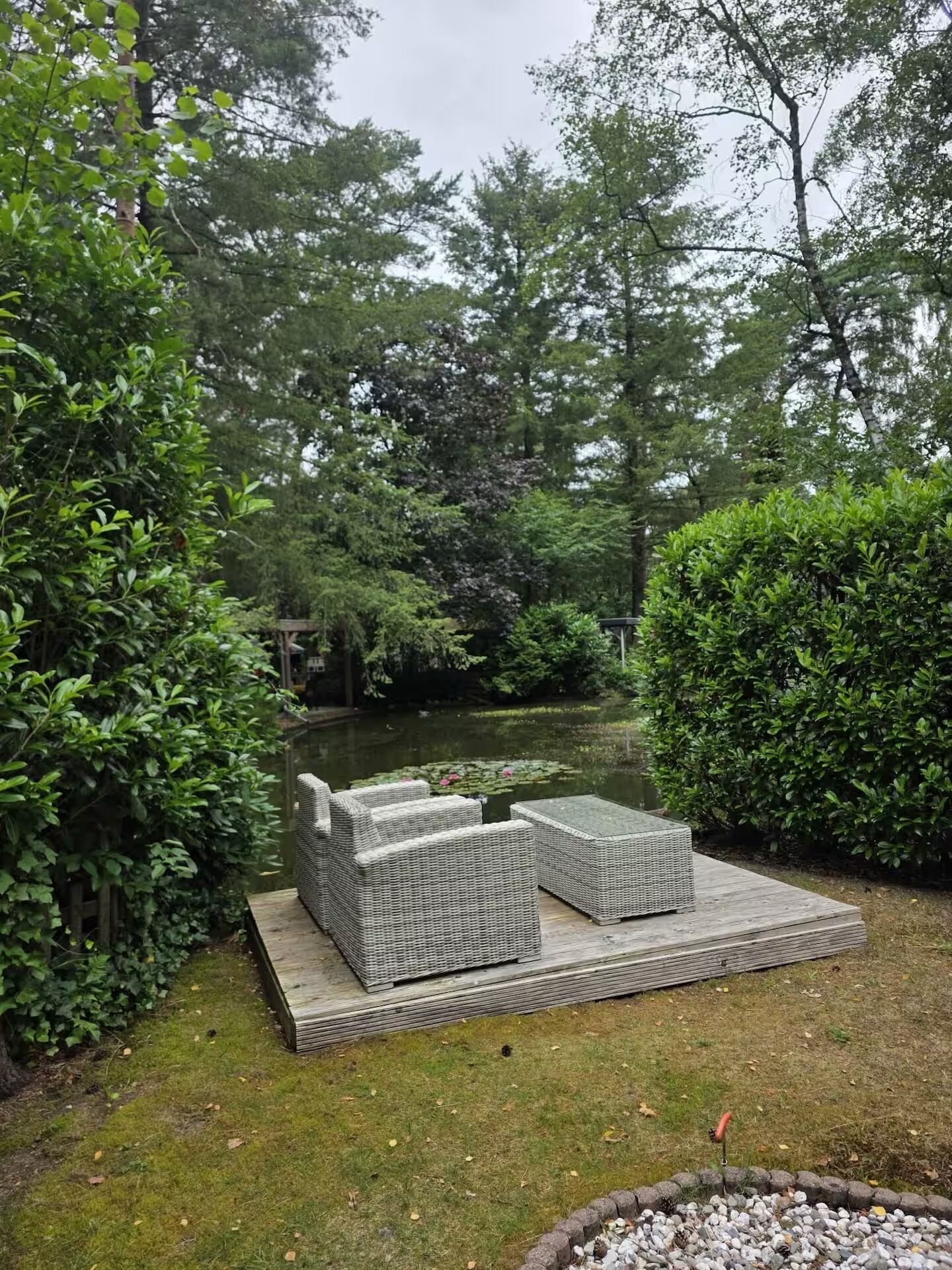 A garden with a pond, wicker furniture, and a wooden deck.