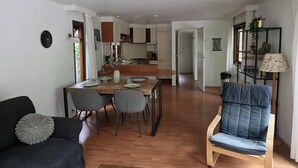 A modern living room with a sofa, a dining table set for four, and a kitchen in the background.