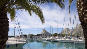 A marina with boats docked, palm trees, and buildings in the background. - 3-Bedroom Apartment with Panoramic Ocean View · 100 m² Terrace · Marina (Villeneuve-Loubet)