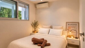 A bedroom with a bed, a nightstand, a potted plant, a framed artwork, and an air conditioning unit. - 3-Bedroom Apartment with Panoramic Ocean View · 100 m² Terrace · Marina (Villeneuve-Loubet)