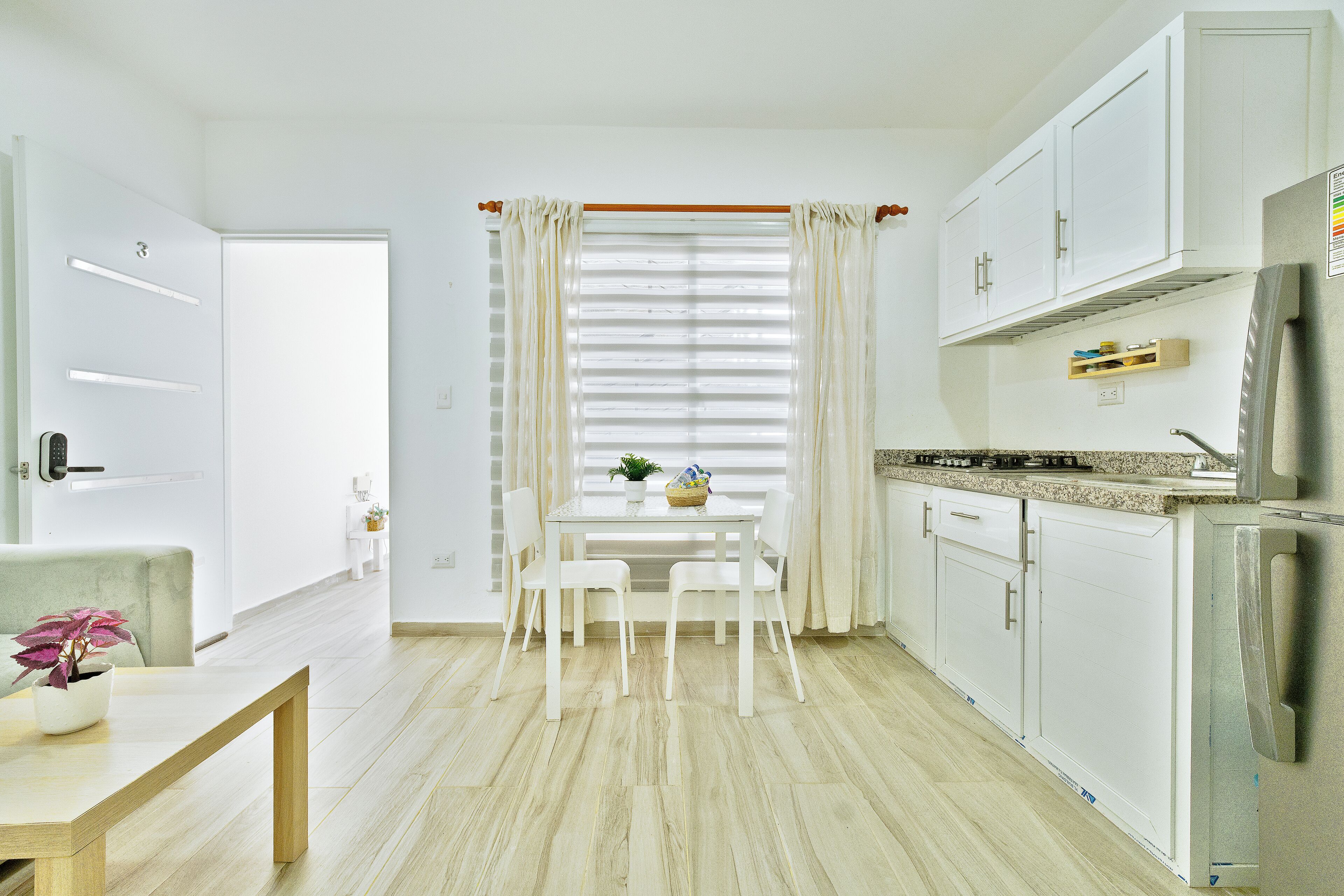 Una cocina moderna con armarios blancos, una mesa de comedor con sillas y una ventana con persianas.