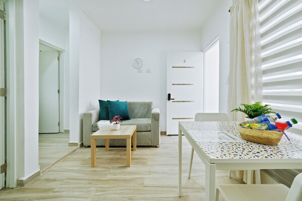 A minimalist living room with a sofa, a small table, and a dining table with a basket of items. - Peaceful 1bedroom studio with AC in charming Cabrera (Cabrera)
