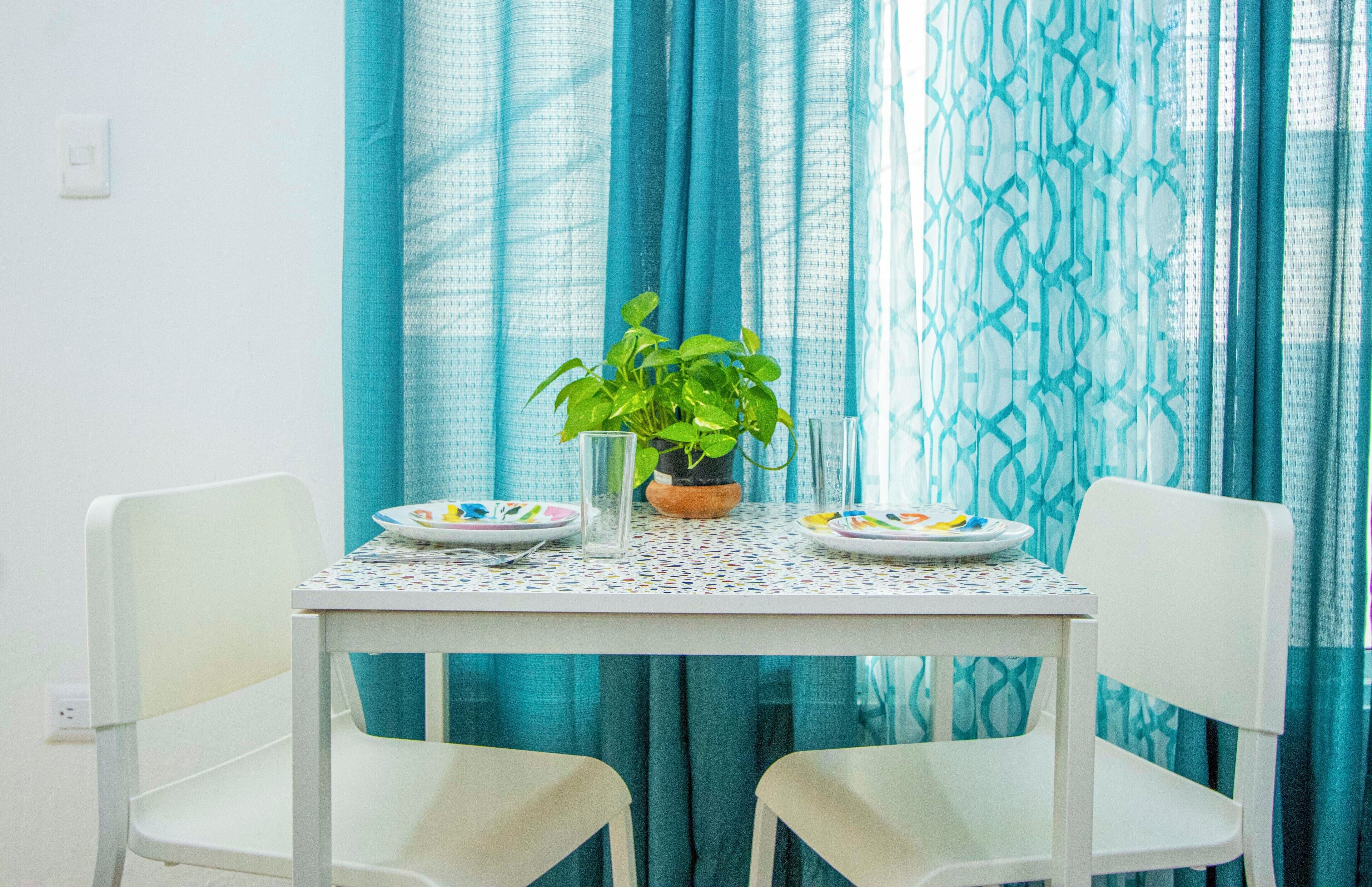 Una mesa de comedor con dos sillas, una planta en maceta y platos con cubiertos.