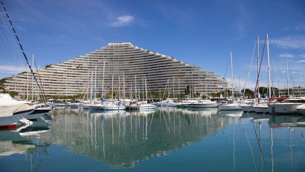A large cruise ship docked at a marina with multiple boats and a large hotel structure in the background. - Ocean and Marina View · Terrace · Sleeps 4 · Riviera (Villeneuve-Loubet)