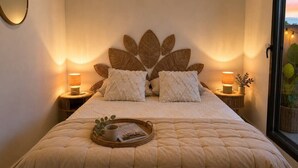 A neatly made bed with a leaf-patterned headboard, two bedside lamps, a tray with a mug and magazine, and a window with a view. - 2-Bedroom Apartment with Private Terrace · Pool · 50m from the Beach · Parking (Villeneuve-Loubet)