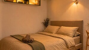 Una cama individual con cabecera, una mesita de noche, una lámpara y una planta.