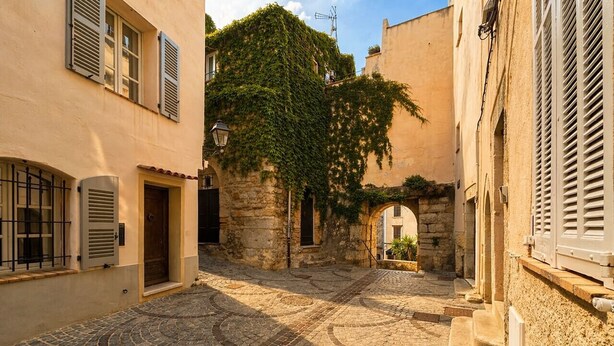 Un patio empedrado con edificios de piedra, una puerta de madera y una ventana con contraventanas.