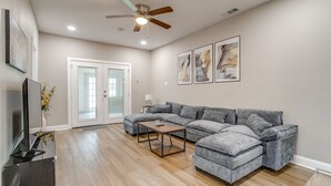 A living room with a sectional sofa, a coffee table, a ceiling fan, and artwork on the wall. - Spacious Dallas Home + Guest House | Sleeps 21 (Dallas)
