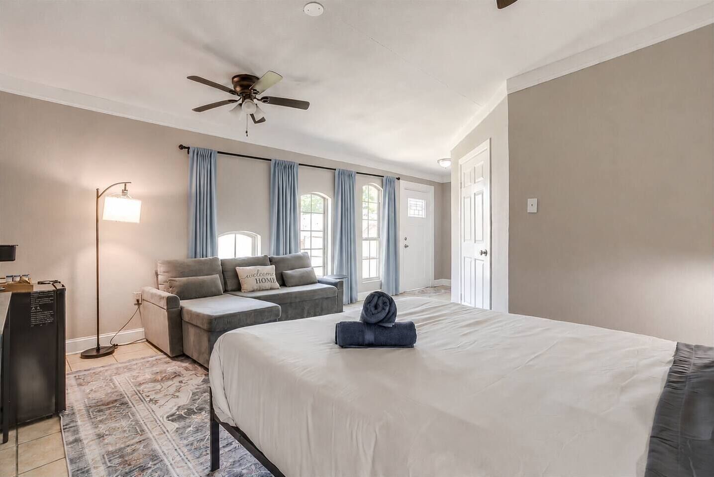 Une chambre à coucher comprenant un lit, un canapé, une lampe sur pied et un ventilateur de plafond.