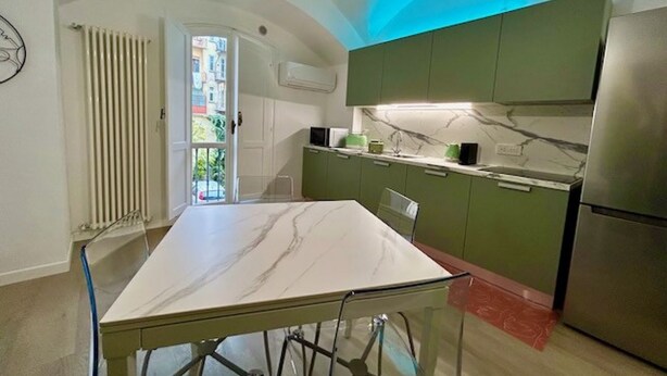 Una cocina con encimera de mármol, armarios verdes y refrigerador de acero inoxidable.