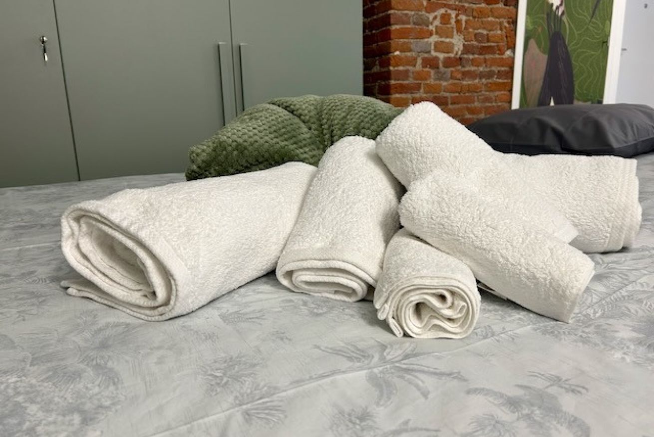 A bed with rolled white towels, a green knitted pillow, and a black pillow.