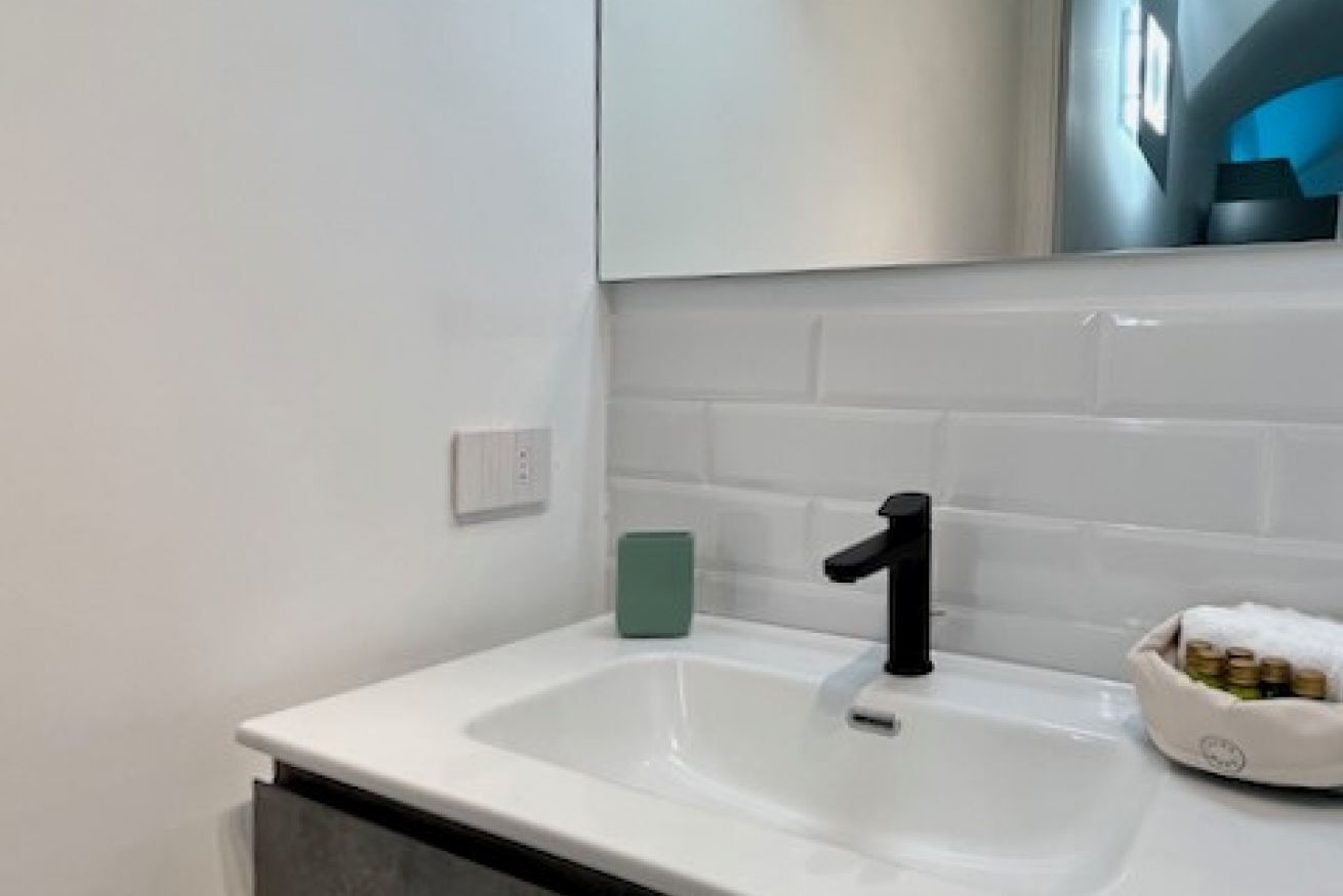 Une salle de bain moderne avec un lavabo blanc, un robinet noir et un porte-savon vert.