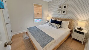 A bedroom with a bed, bedside tables, a ceiling fan, a window with blinds, and a patterned wall. - Fully Furnished Brand-New 3BR/2.5BA Home ~ Hot Tub ~ Close to Airport (Wilmington)