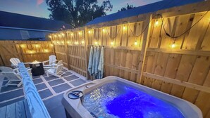 A hot tub with a blue light, surrounded by wooden deck chairs and a wooden fence with string lights. - Fully Furnished Brand-New 3BR/2.5BA Home ~ Hot Tub ~ Close to Airport (Wilmington)