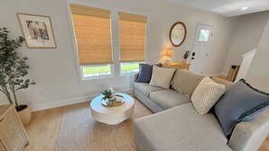 A living room with a sofa, a round coffee table, a potted plant, and a framed picture on the wall. - Fully Furnished Brand-New 3BR/2.5BA Home ~ Hot Tub ~ Close to Airport (Wilmington)