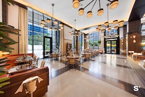 Eine großzügige Hotelhalle mit mehreren Gastronomiebereichen, großen Fenstern und modernen Leuchten.