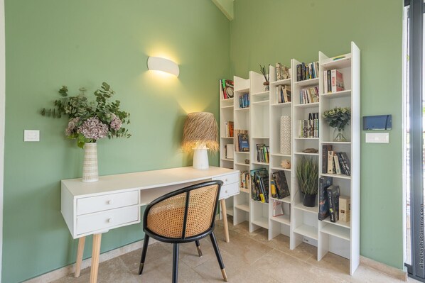 A room with a white desk, a chair, a bookshelf, and a wall-mounted lamp.
