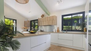 Een moderne keuken met witte kasten, een houten aanrechtblad en een groot raam met uitzicht op een tuin.
