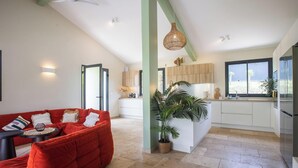 Een ruime woonkamer met een rode bank, een grote potplant en een keuken met houten kastjes.