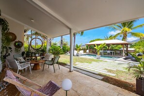 A covered patio with a pool, outdoor seating, and lush greenery. - Contemporary Bohemian-style villa in Stanting with a pool and tropical garden (Le François)