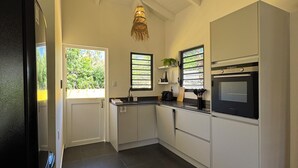 A modern kitchen with white cabinets, a black refrigerator, a built-in oven, and a hanging light fixture. - Bungalow, Casita Apapacho, Shared swimmingpool, Jan Thiel, 15kWh p.n. Included (Jan Thiel)