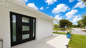 Une maison moderne avec une porte d’entrée noire, une façade blanche et un petit jardin agrémenté d’un pot bleu.