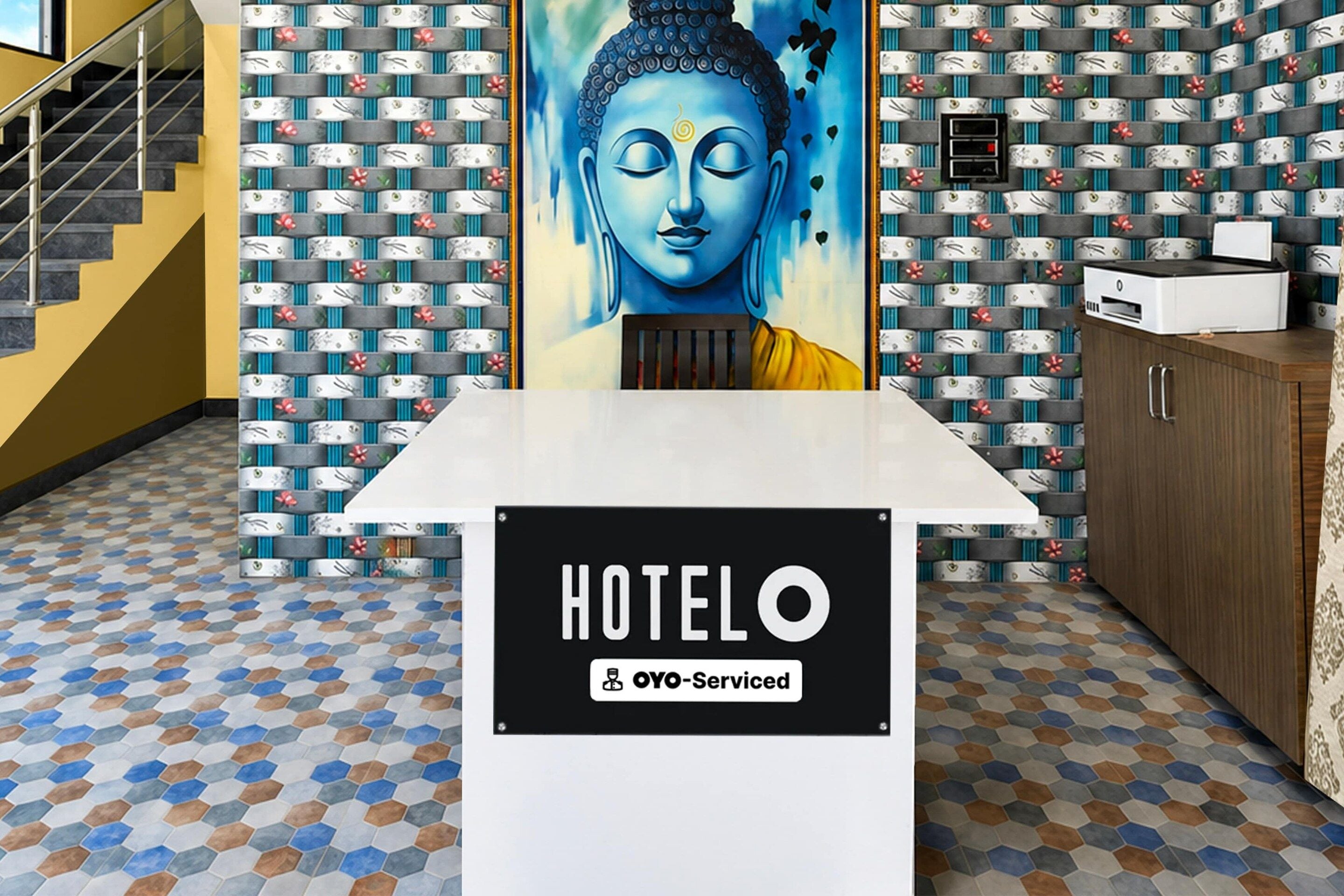 Una recepción con un cartel que dice 'HOTEL' y 'OYO-Serviced' en una habitación con papel tapiz estampado y un diseño geométrico en el suelo.