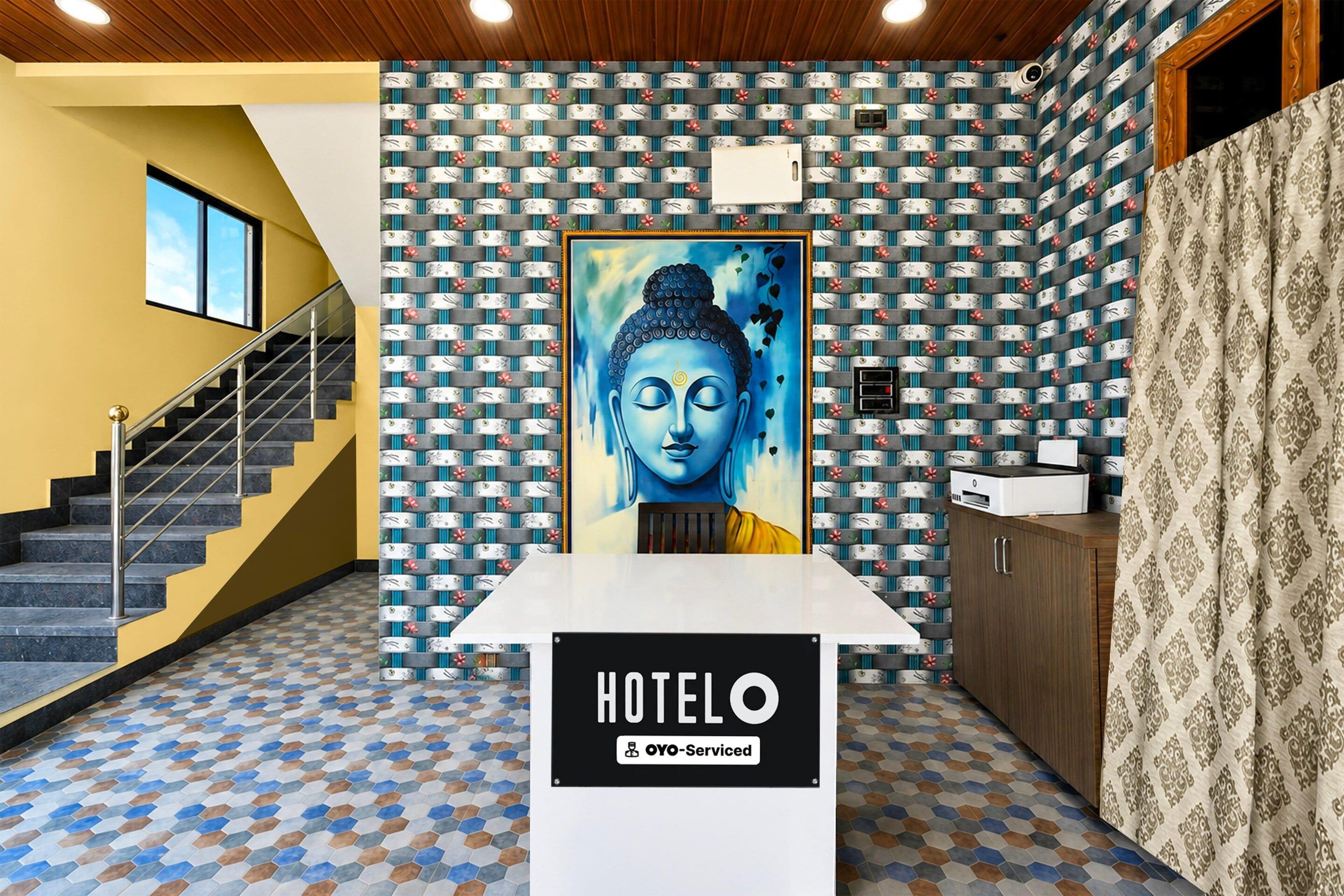 A hotel reception area with a Buddha statue, a staircase, and a patterned floor.