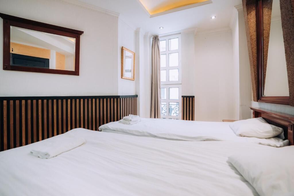 Habitación de hotel con dos camas, un ventanal grande, un espejo y un cabecero de madera.