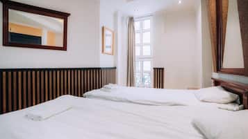 Habitación de hotel con dos camas, un ventanal grande, un espejo y un cabecero de madera.