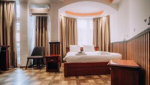 Une chambre d’hôtel avec un lit, une chaise, une table de chevet, un plancher en bois et une fenêtre avec des rideaux.