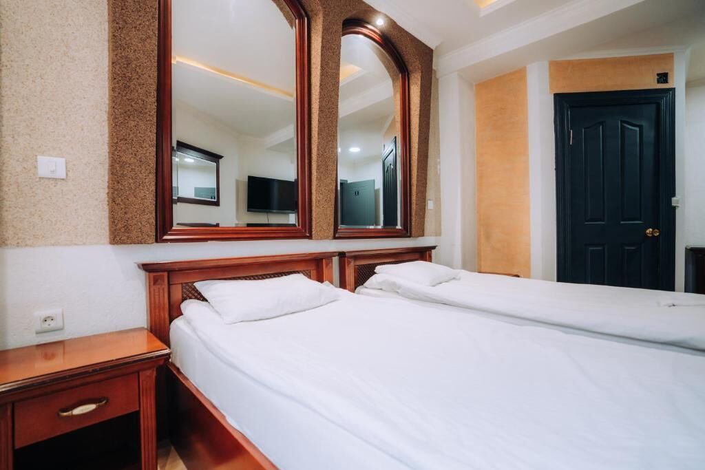 A hotel room with two single beds, a large mirror, a wooden nightstand, and a black door.